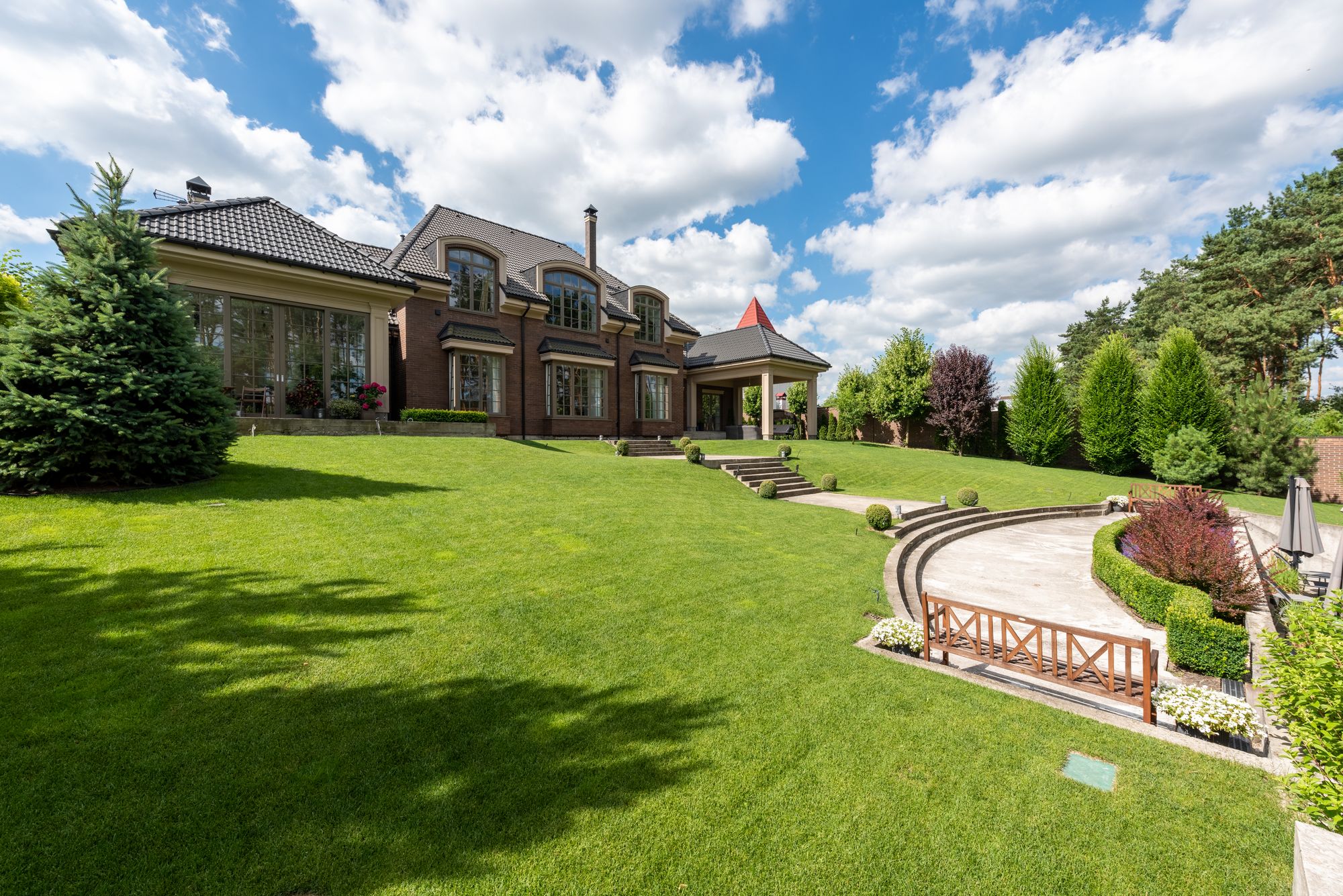 Grand two-story brick luxury home with tall windows, landscaped gardens, and a sweeping green lawn
